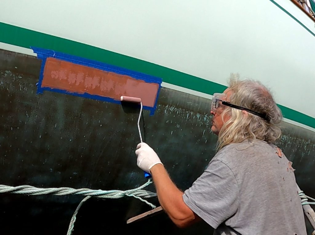 A man holding a roller applying Coppercoat to a boat's hull