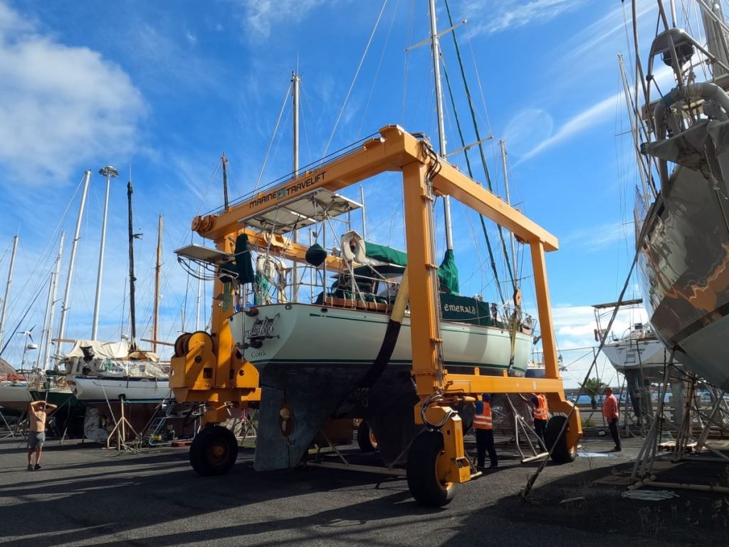 A yellow boat crane surrounding a sail boat as it prepares to be picked up and taken to be launched
