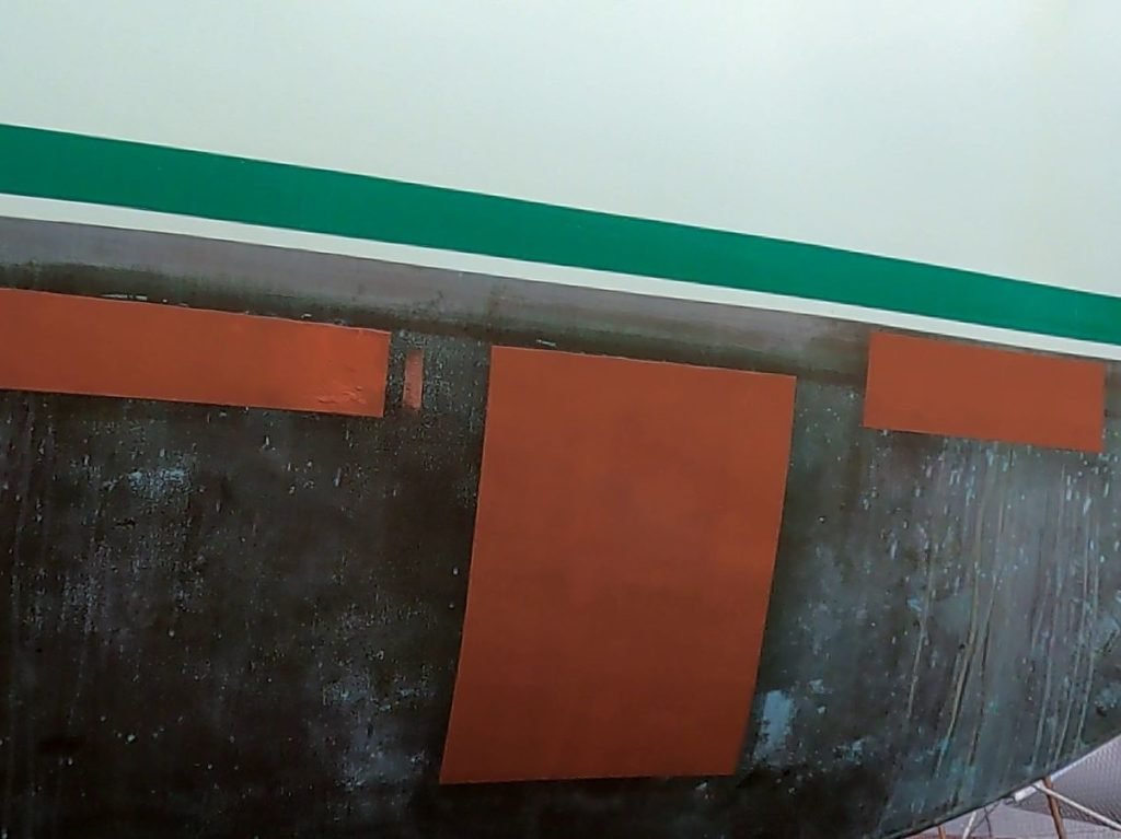 A section of a boat's hull showing three patches of bright now Coppercoat against the old