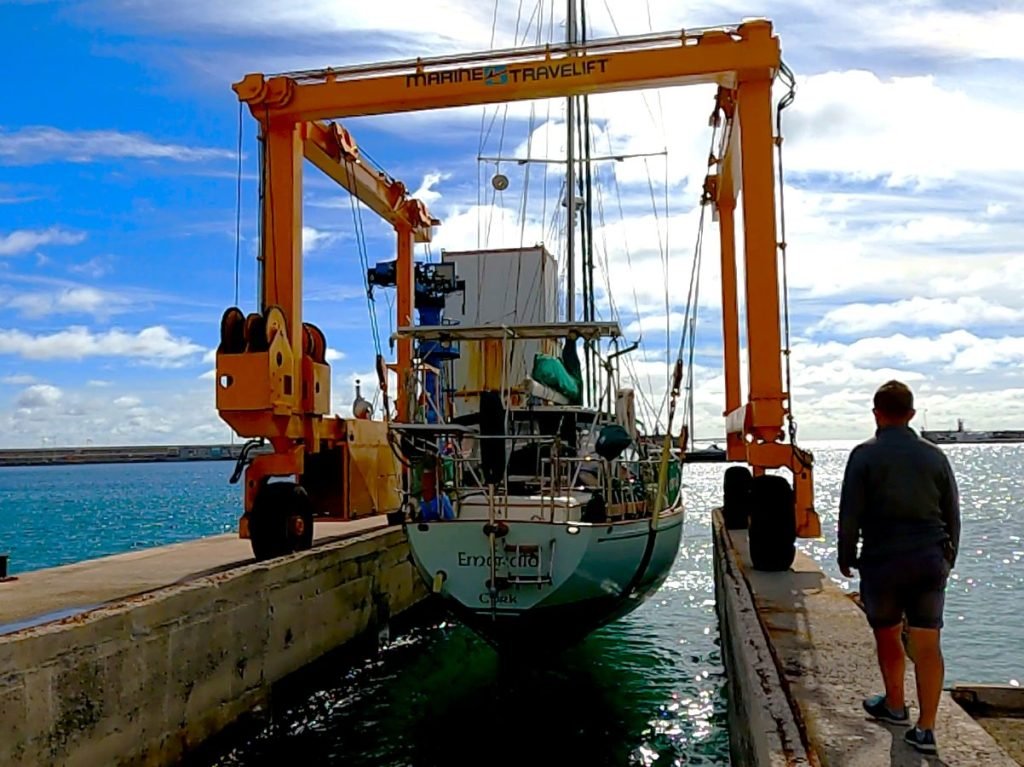 A yellow boat crane launches a sailing boat into the water