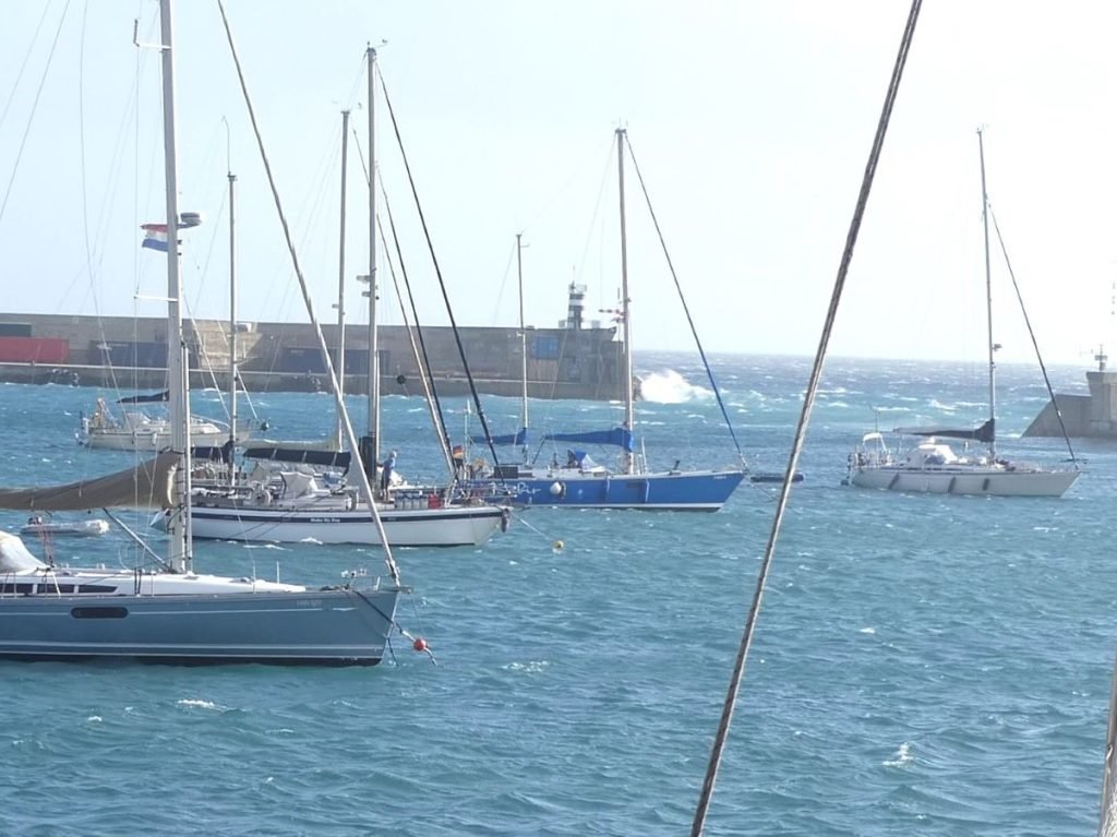 Boats at anchor in Porto Santo with a choppy sea and waves outside the harbour entrance